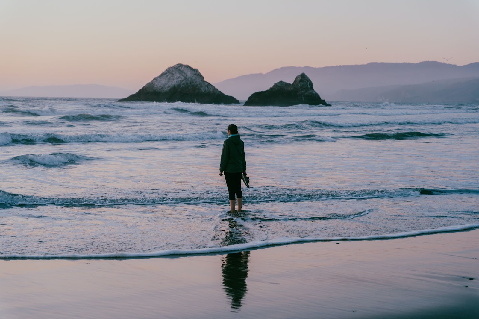 sea sea shore at sunset with gentle waves and a girl entering the water on the sandy shore. mountain silhuettes in the background