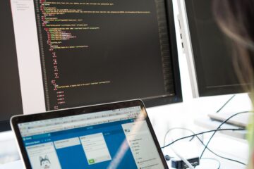 A photo of a laptop in front of two screens showing remote tech support work being done