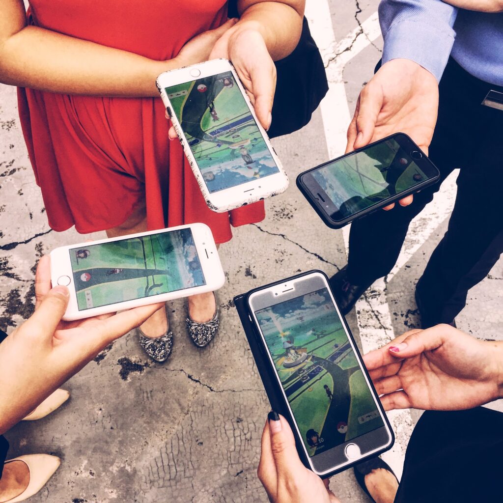 A photo of 4 people, holding out their phones, showing they are playing a game on them.